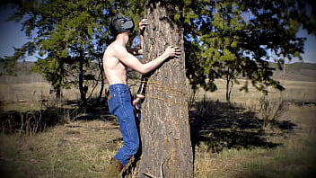 Horny twink in a dark mask fucks a sex toy that is to a tree in a public wilderness.